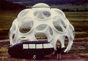 Image of Buckminster Fuller standing next to a concept dome and the Dymaxion Car.